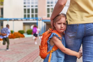 young girl clinging to mothers leg